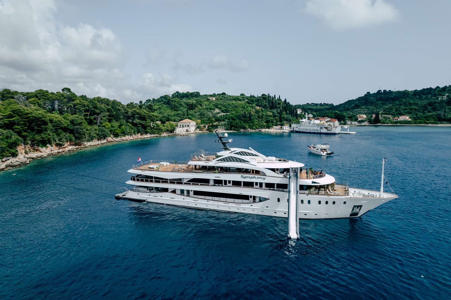 Croatian mini cruiser Symphony at anchor in a green, wooded bay with a water slide off the stern
