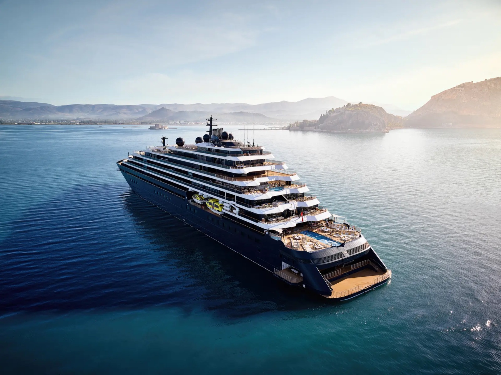 The Ritz-Carlton Yacht Collection's Evrima anchored off a rocky coastline at sunrise